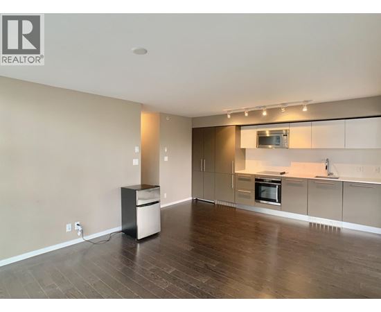 A spacious living room with a kitchen area in the background.