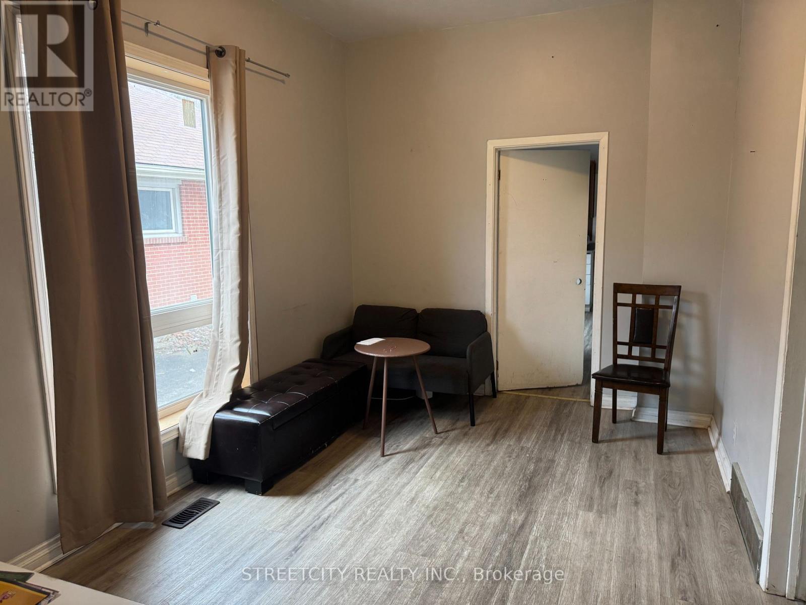 A living room with a black ottoman, a small table, and a chair.