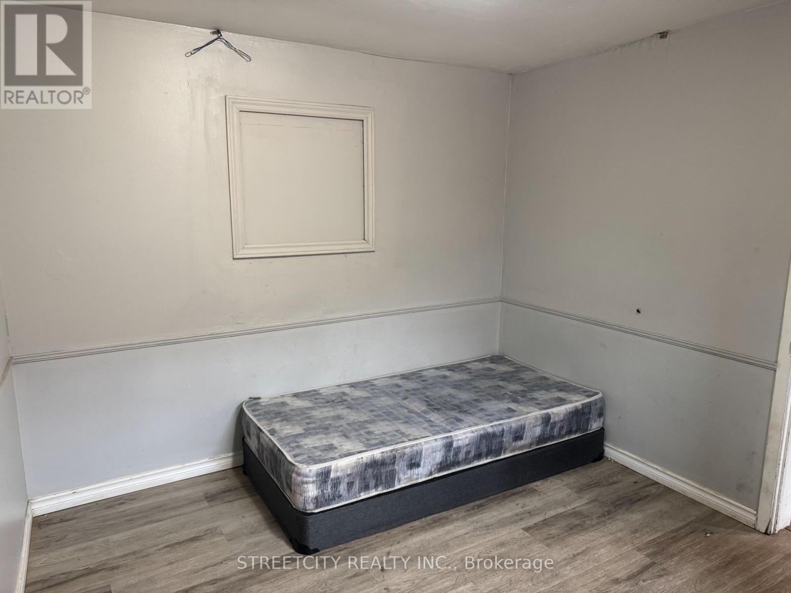 A bedroom with a bed, wooden floor, and a picture frame on the wall.
