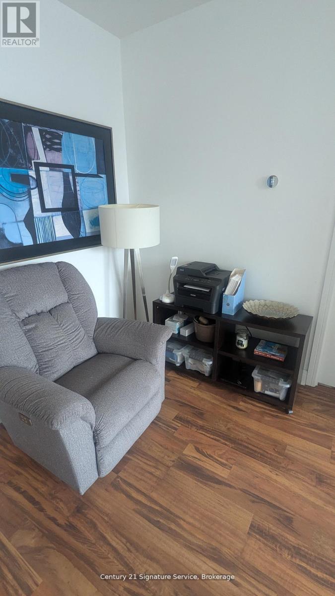 A grey couch sits in a living room with a lamp and a painting on the wall.