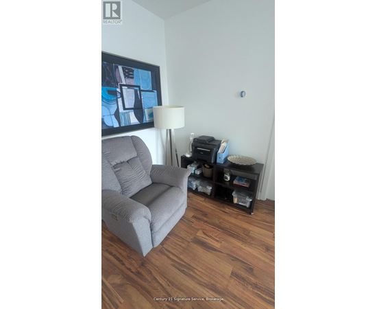 A grey couch sits in a living room with a lamp and a painting on the wall.