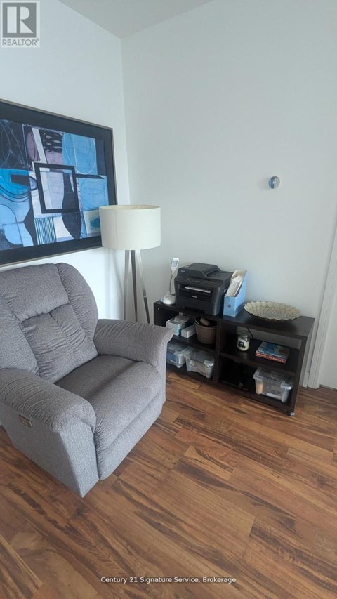 A grey couch sits in a living room with a lamp and a painting on the wall.