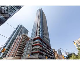 A tall building with a glass facade stands in front of other buildings.