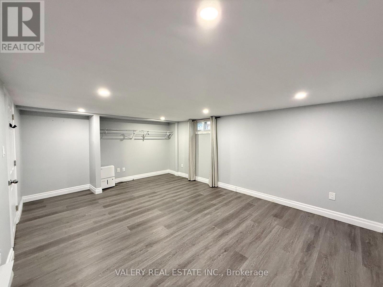 A spacious room with wood flooring and white walls.
