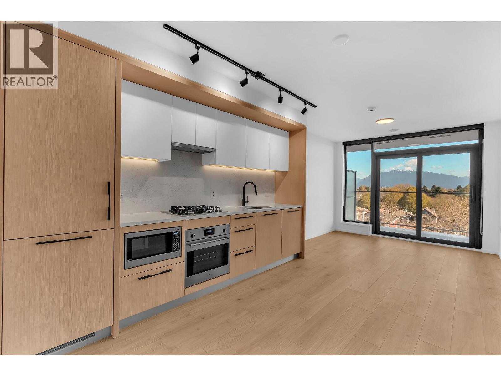 A modern kitchen with wooden cabinets and a large window overlooking a mountainous landscape.
