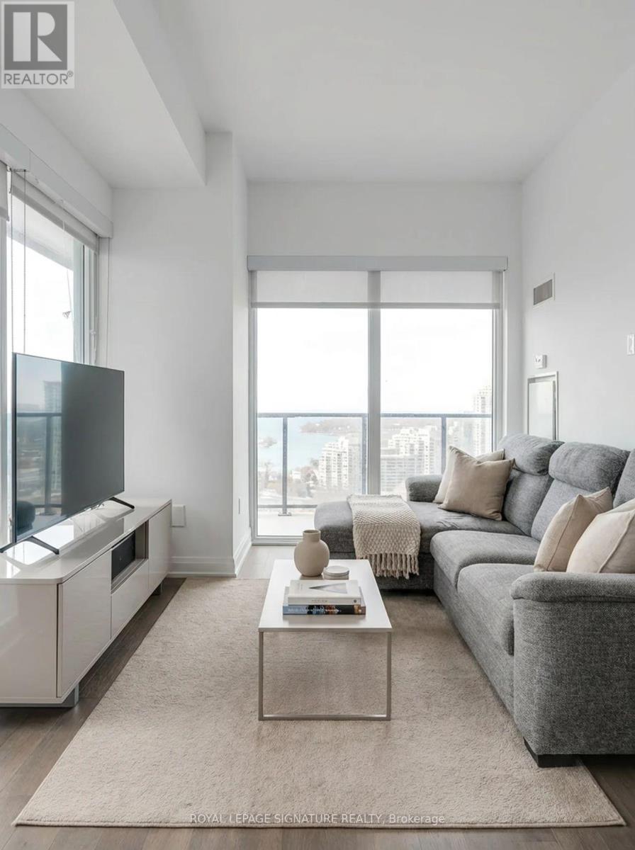A living room with a grey couch, a white entertainment unit, and a large window.