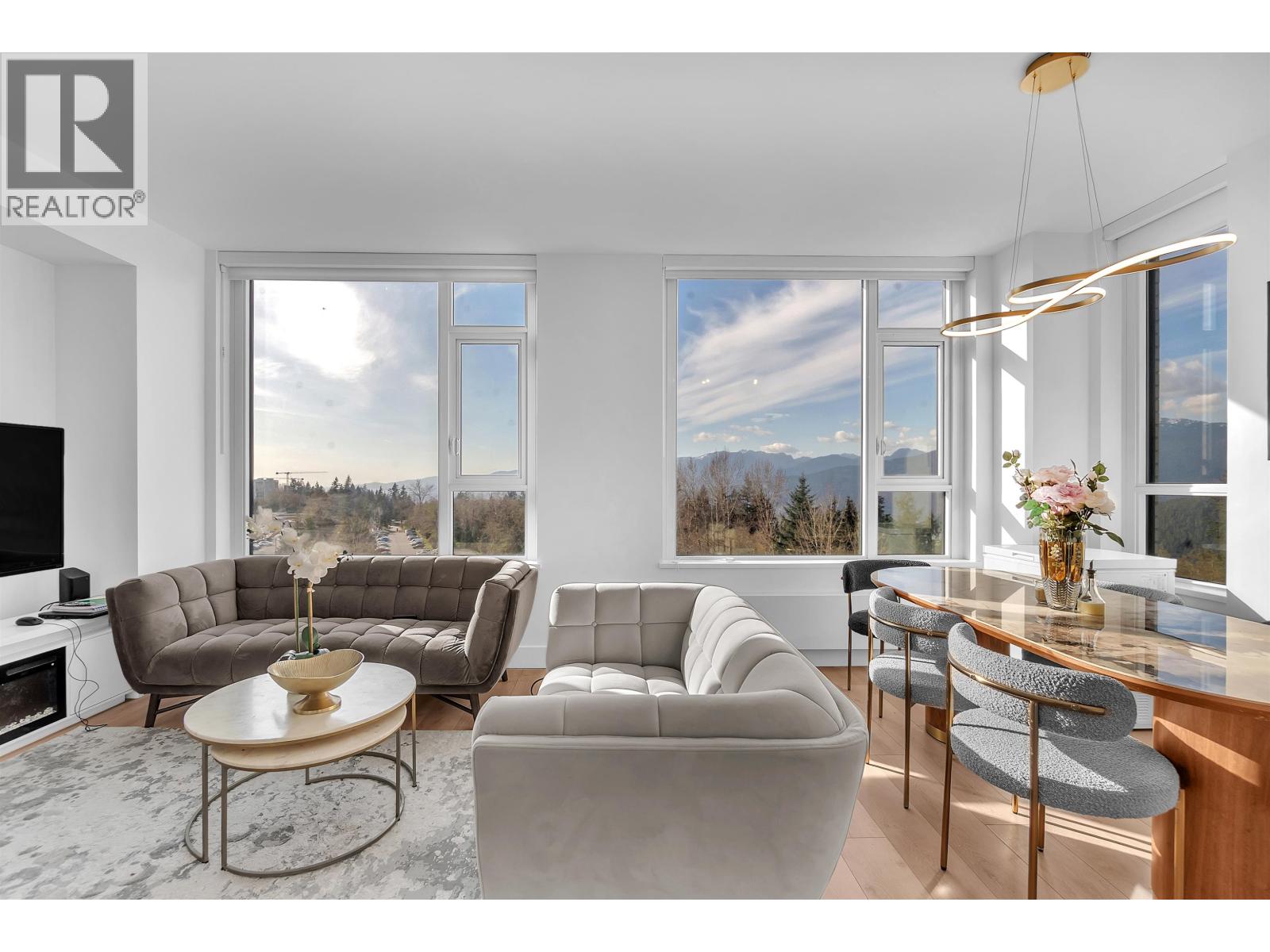 A living room with a grey sofa, a coffee table, and a large window with a view of the mountains.