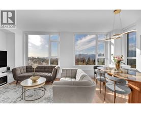 A living room with a grey sofa, a coffee table, and a large window with a view of the mountains.