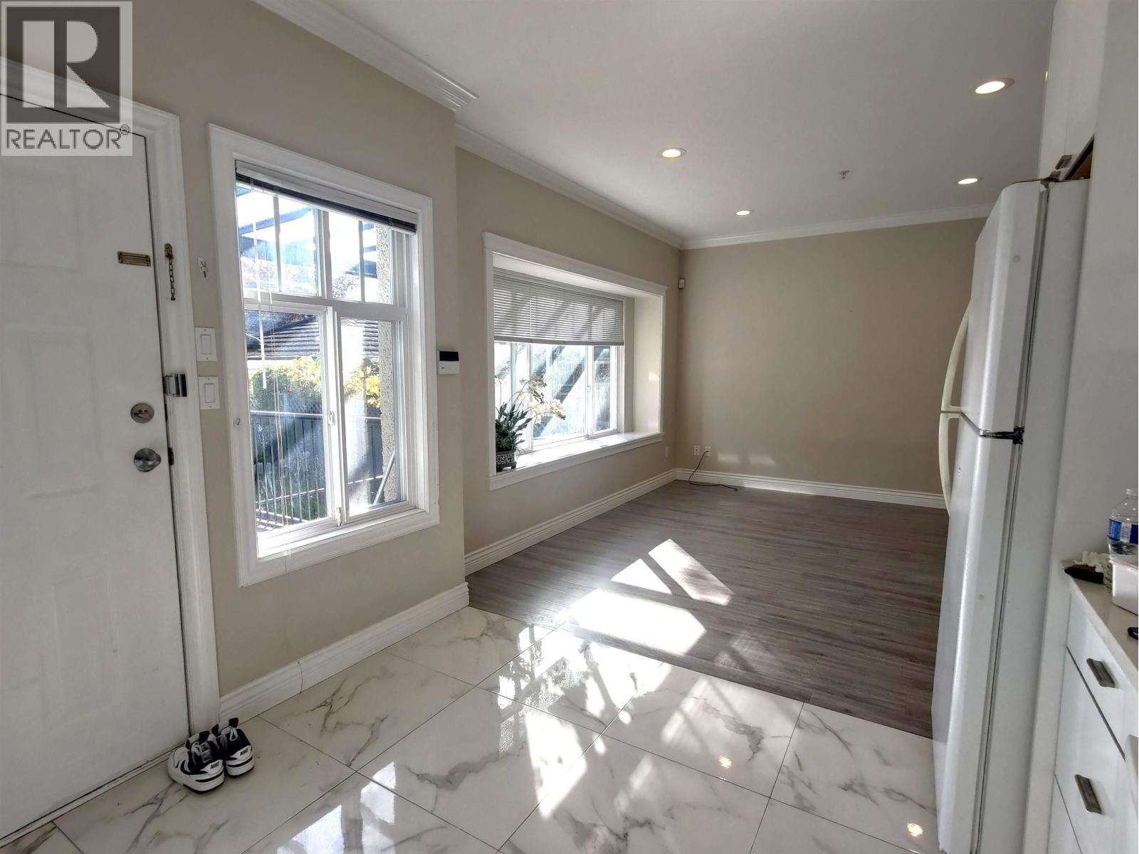 A spacious kitchen with white marble flooring and a refrigerator on the right side.