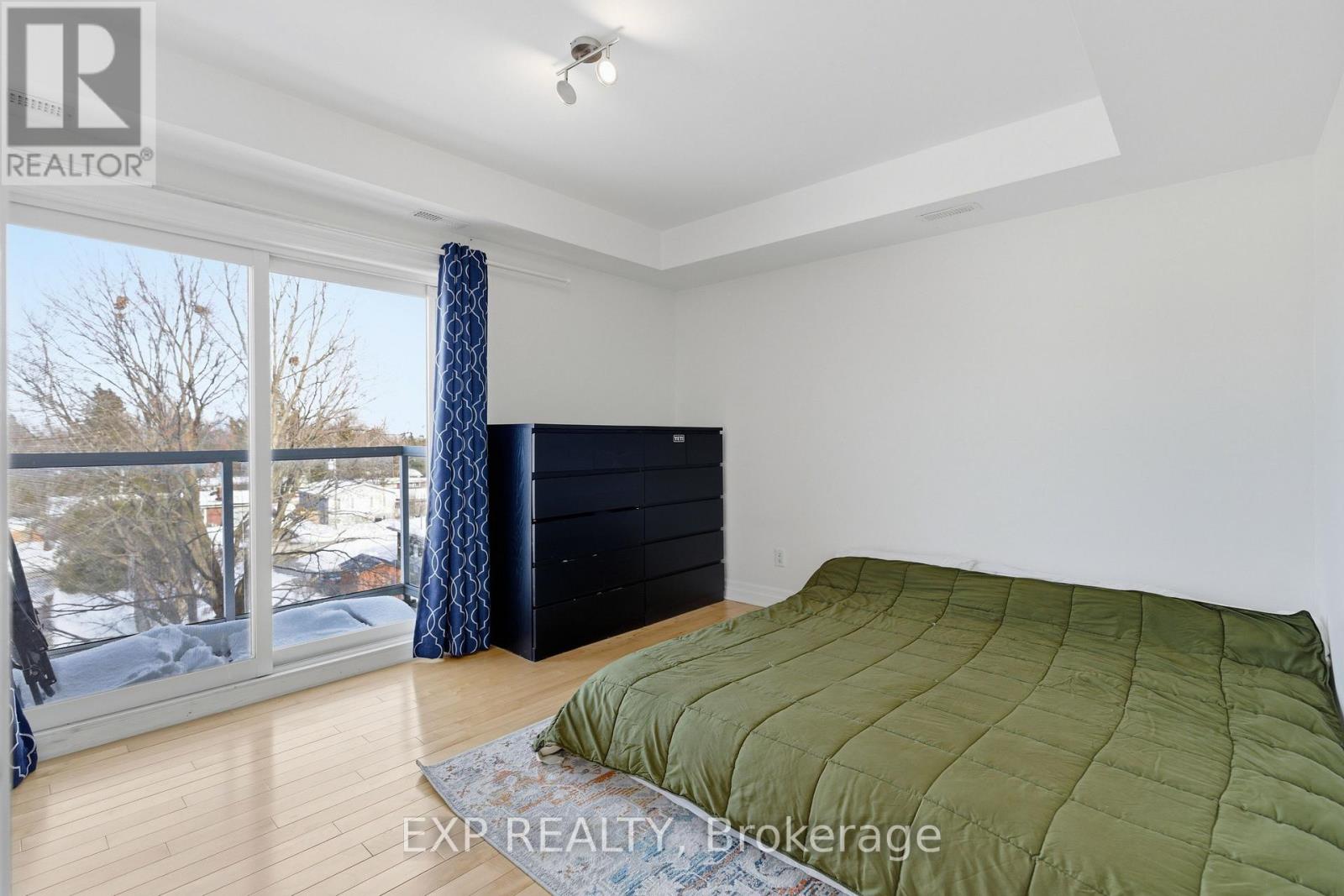 A bedroom with a large bed and a balcony with a view of trees and houses.