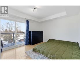 A bedroom with a large bed and a balcony with a view of trees and houses.
