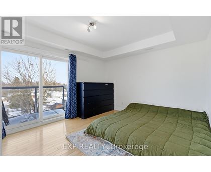 A bedroom with a large bed and a balcony with a view of trees and houses.
