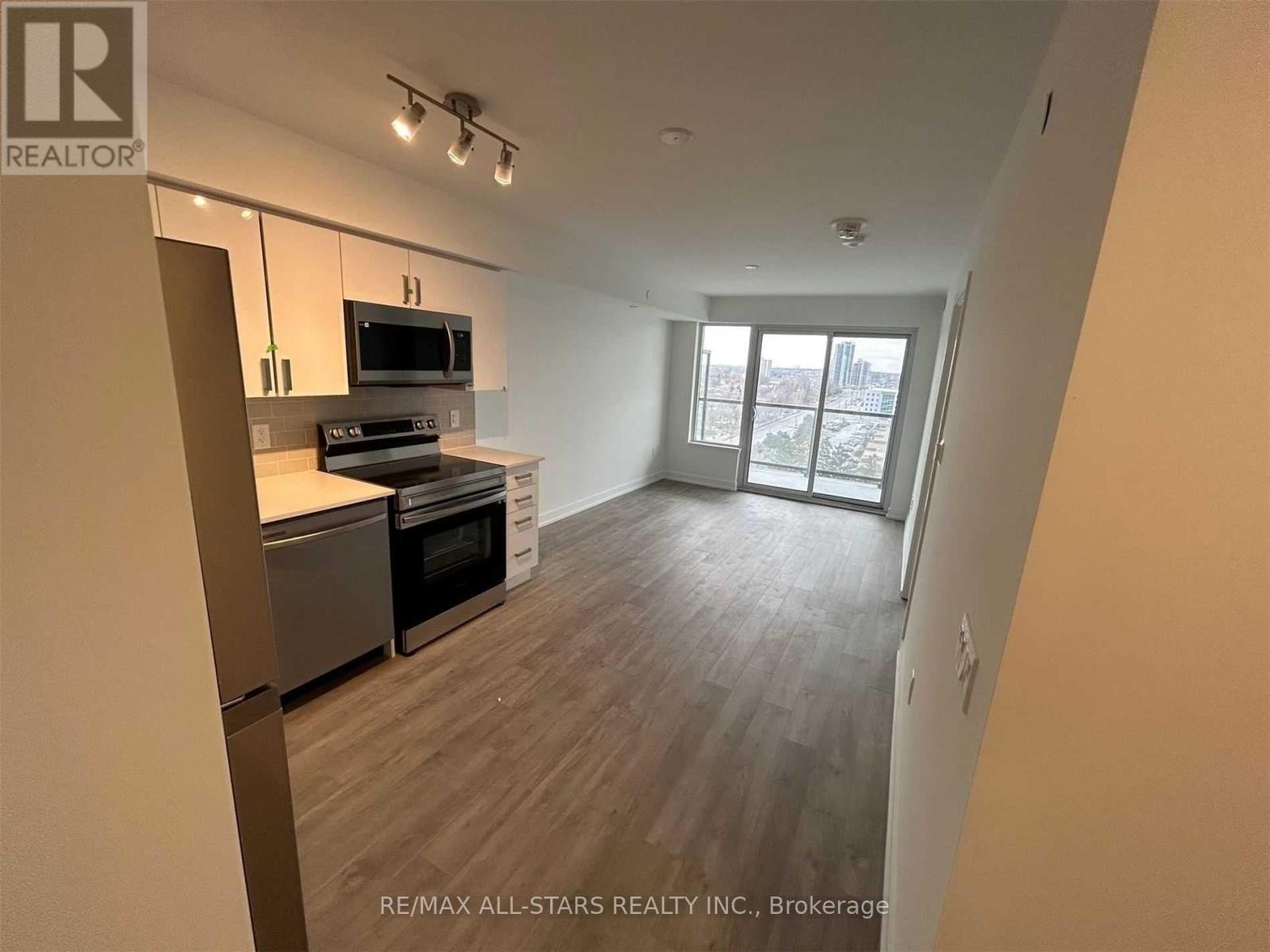 A spacious living room with a kitchen area and a view of the city through the windows.