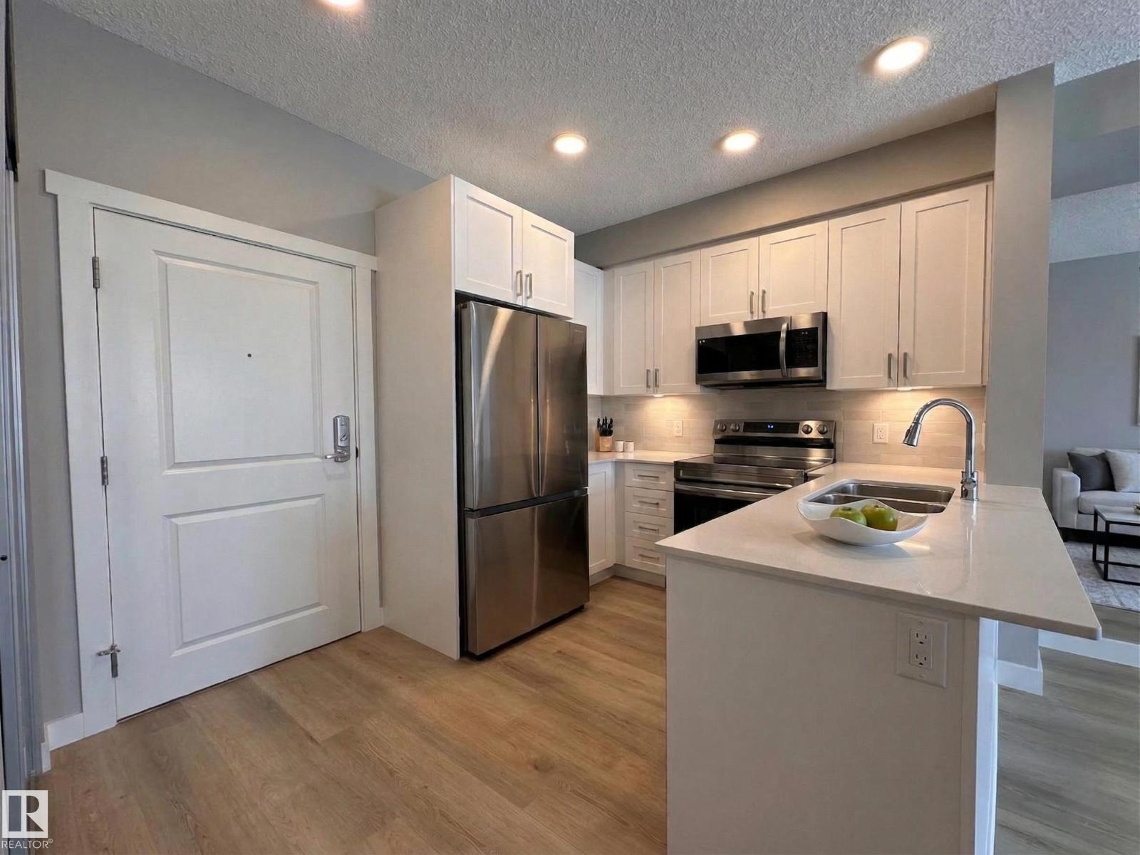 A kitchen with a refrigerator, microwave, oven, and sink.