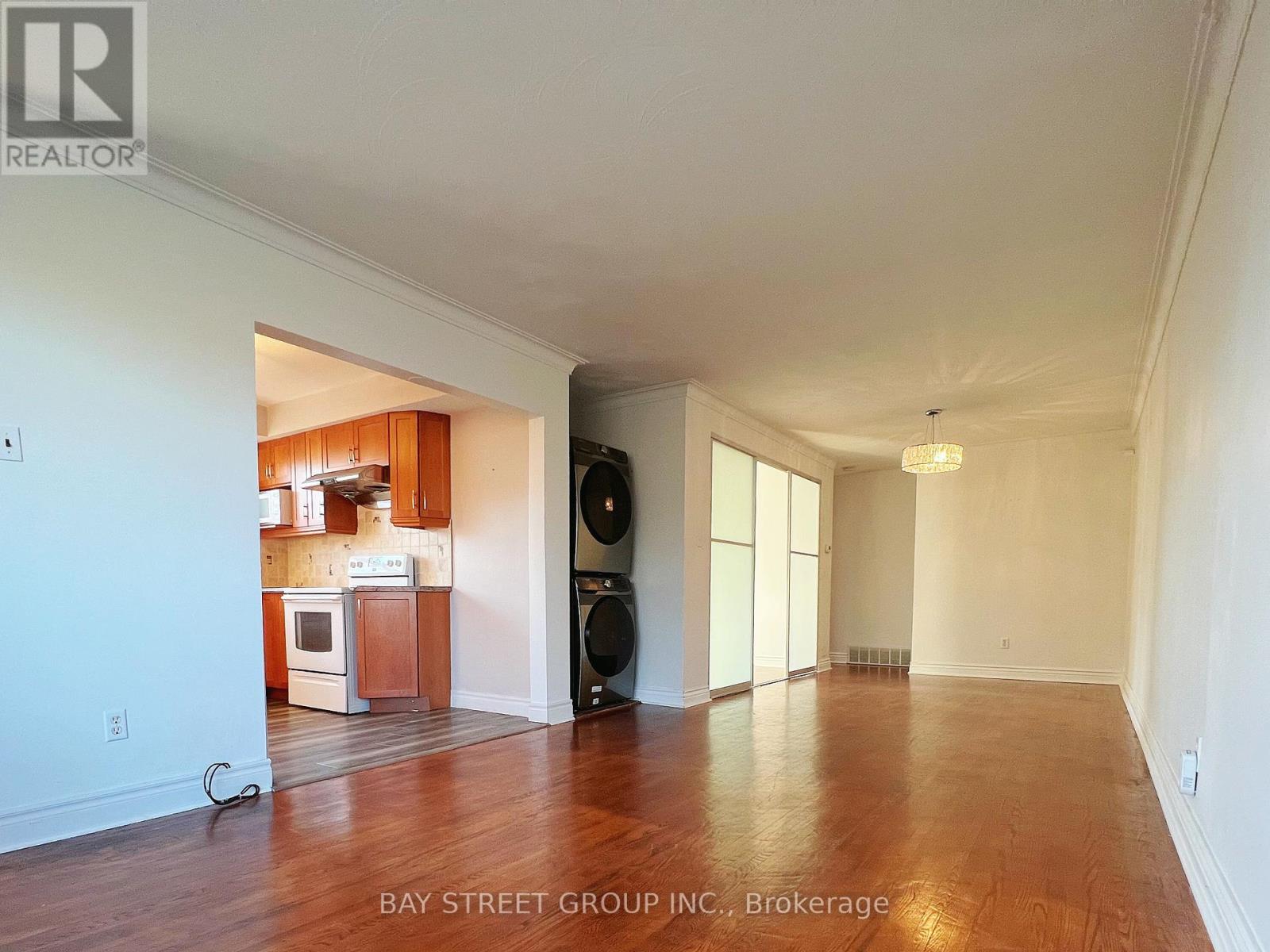 A spacious room with wooden floors and a kitchen area in the background.