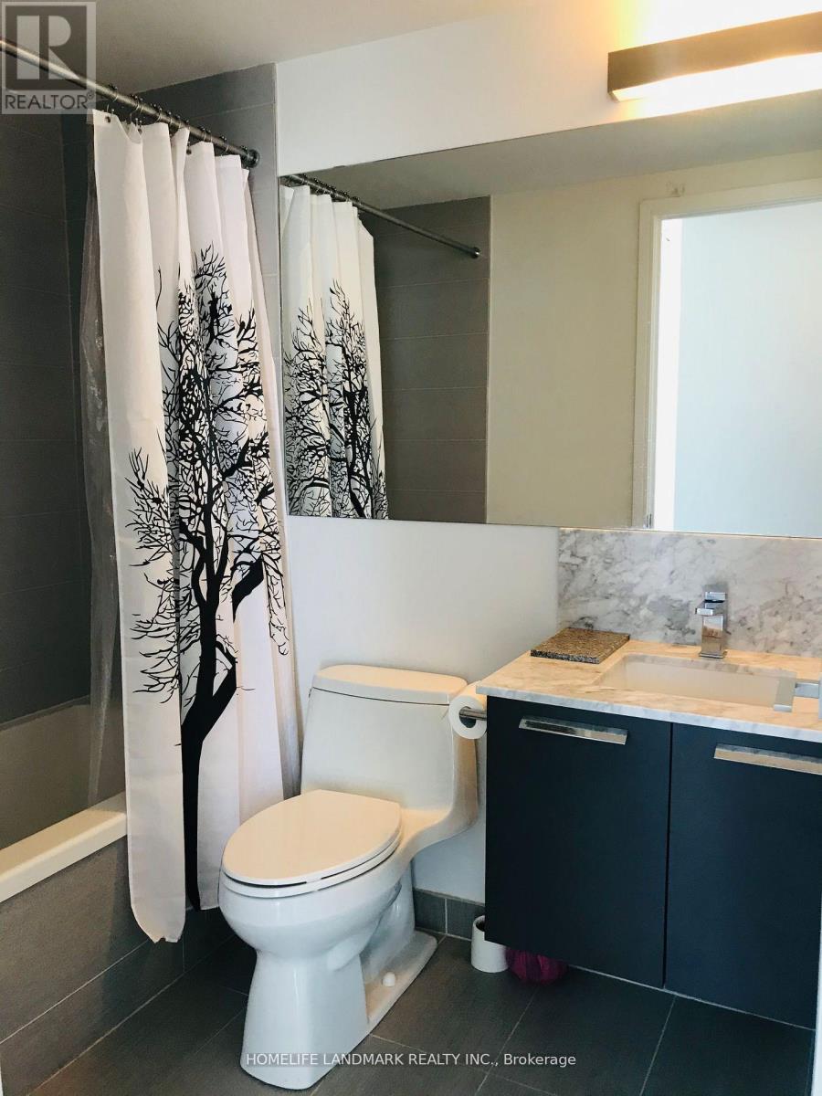 A white toilet with a tree patterned shower curtain in a bathroom.