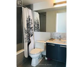 A white toilet with a tree patterned shower curtain in a bathroom.