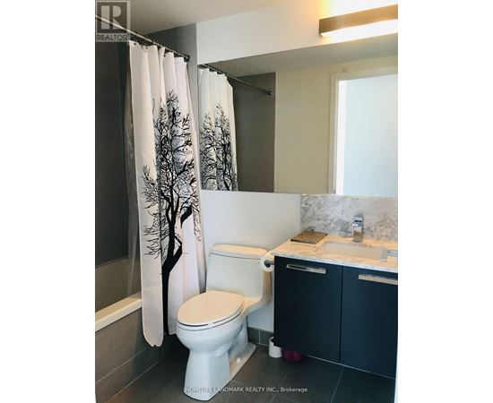 A white toilet with a tree patterned shower curtain in a bathroom.