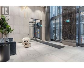 The image shows a modern office lobby with a reception desk, a potted plant, and a bench.