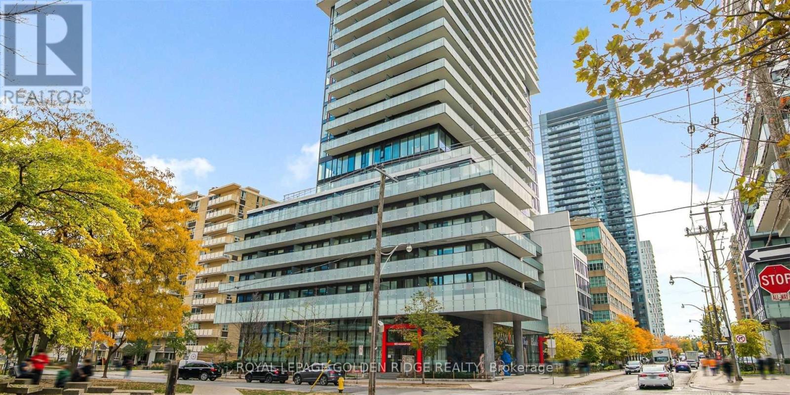 A tall building with a glass facade stands in the middle of a street lined with trees.