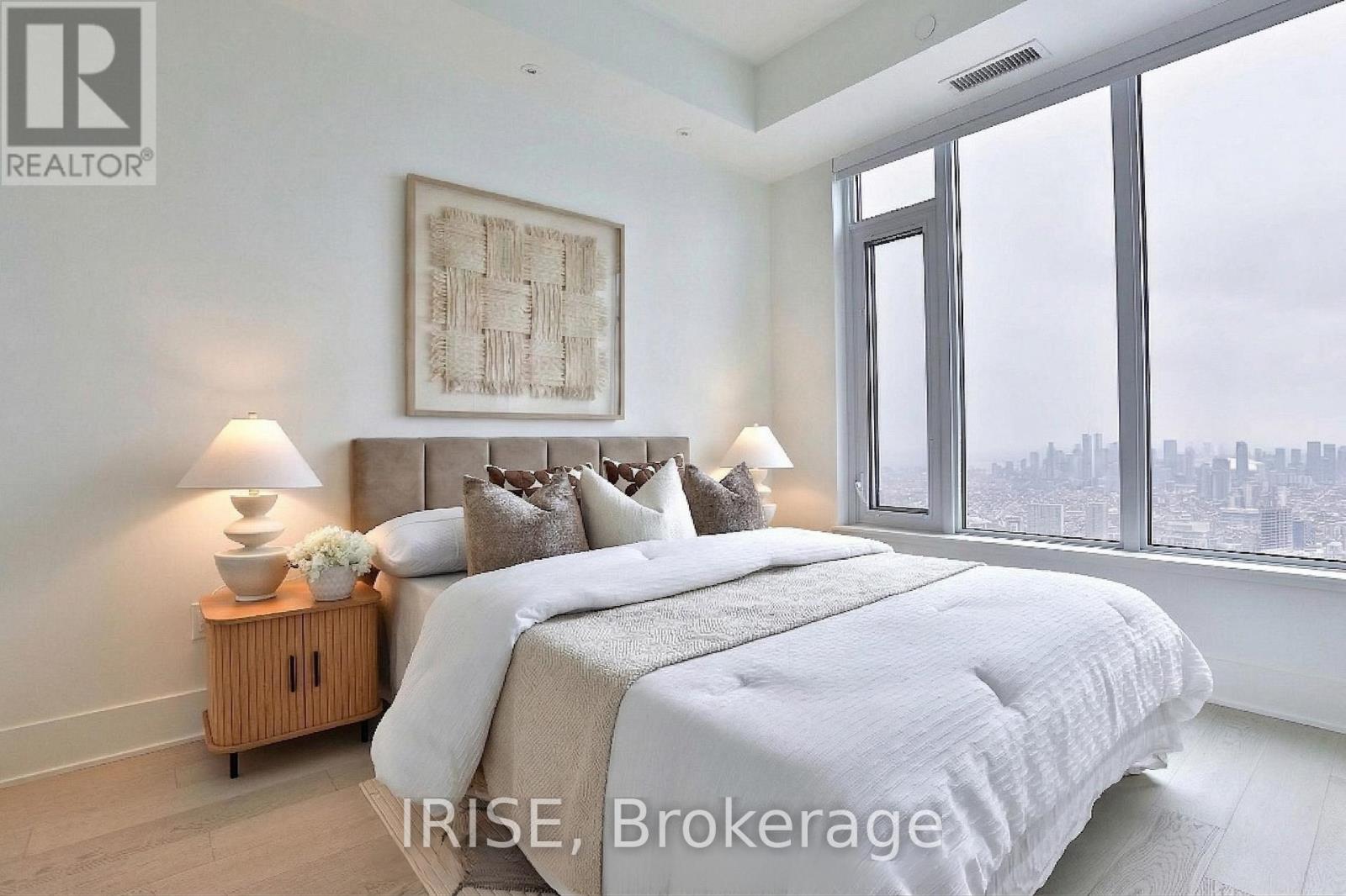A bedroom with a large bed and a city view through the window.