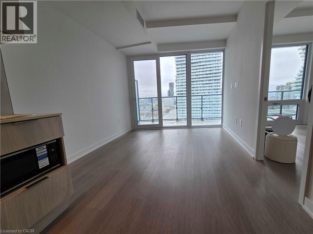 A spacious room with wooden flooring and a large window with a view of the city.