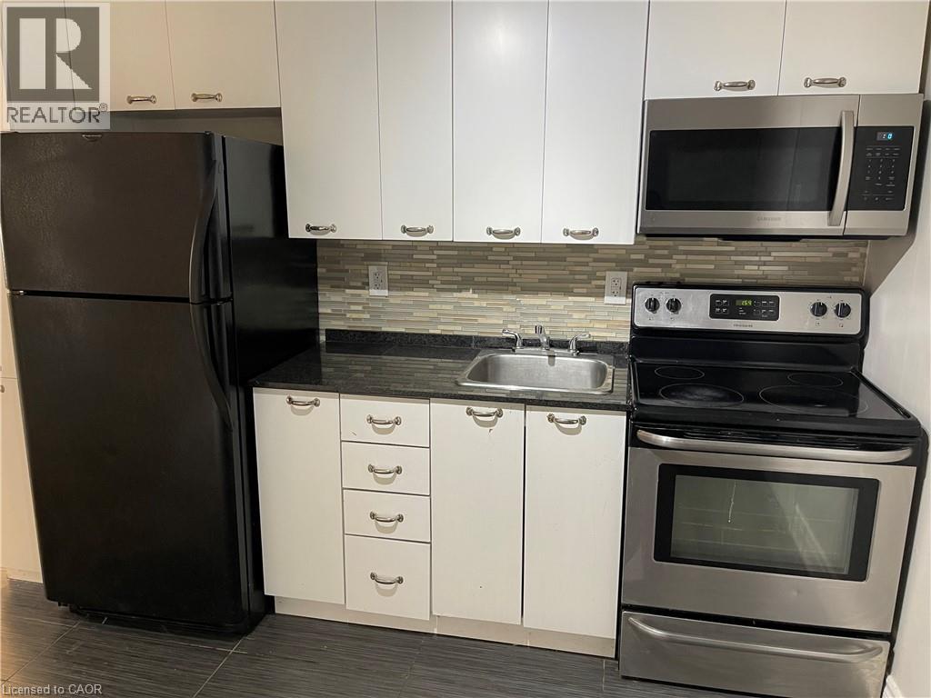 A black refrigerator is in a kitchen with white cabinets.