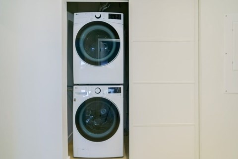Two washing machines are stacked on top of each other in a small space.