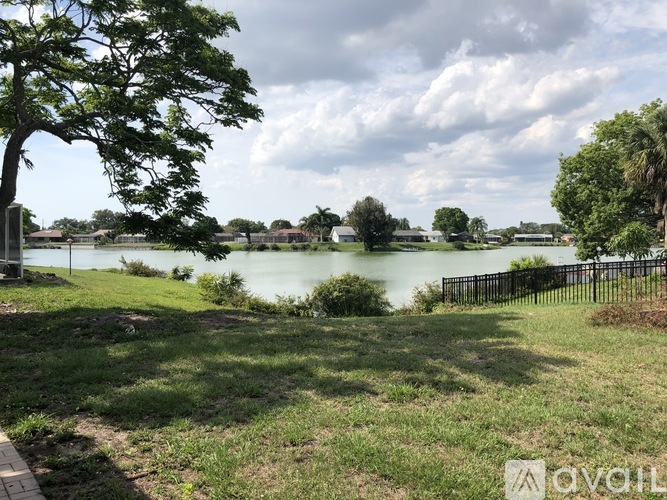 A park with a lake, trees, and a fence.