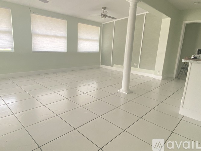 A spacious room with white tiled flooring and a ceiling fan.