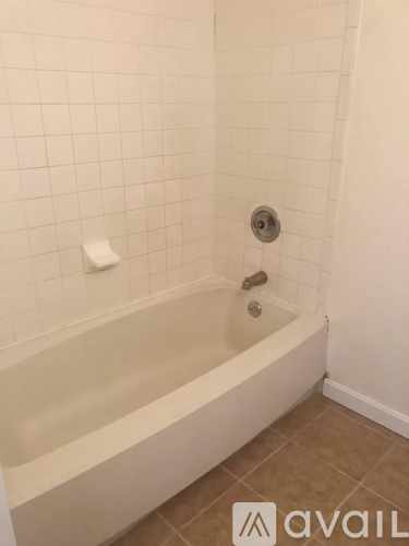 A white bathtub with a shower head and a roll of toilet paper on the wall.