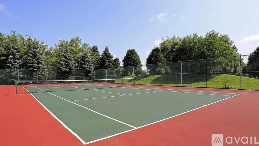 A tennis court with a green and red surface surrounded by a fence and trees.