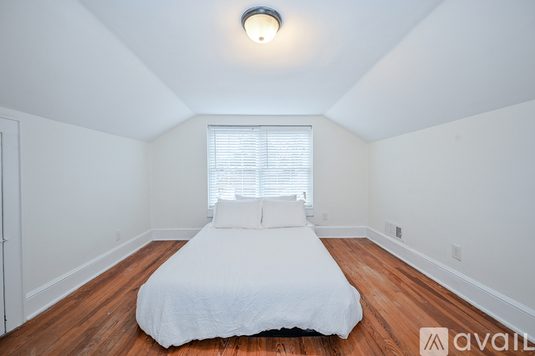 A bedroom with a bed, wooden floor, and a window with blinds.