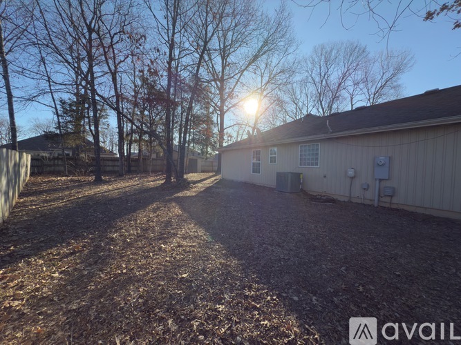 A backyard with a house, trees, and a gravel ground.