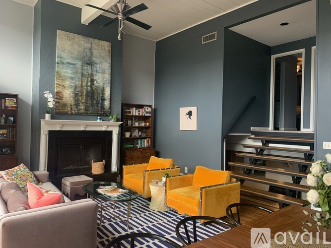 A living room with a fireplace, a painting, a bookshelf, a chair, a coffee table, and a vase of flowers.