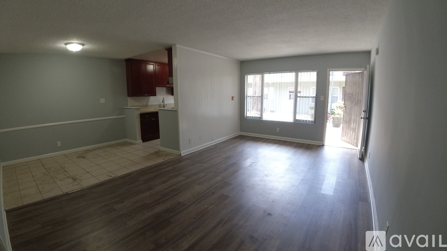 A room with wooden floors and a kitchen area in the background.