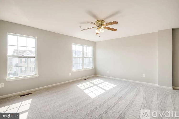 A spacious room with a ceiling fan and two windows.