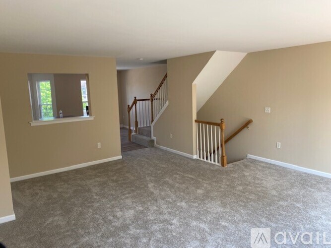 A spacious room with a carpeted floor, a staircase with wooden railings, and a window with a view of trees outside.