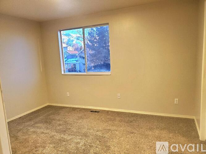 A room with a carpeted floor and a window showing a view of trees and buildings outside.