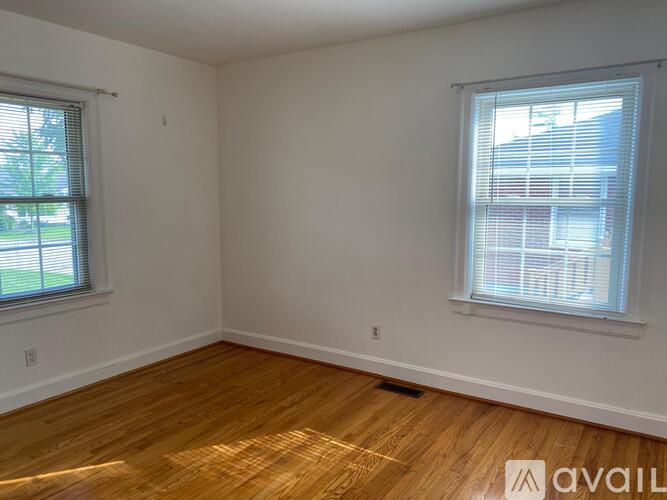 A room with wooden flooring and two windows.