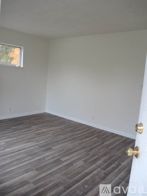 A room with a wooden floor and a white wall with a window.