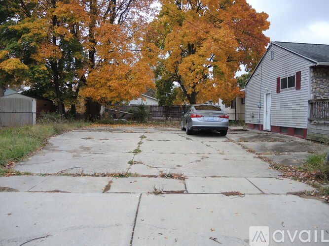 A car is parked in a driveway with a house and trees in the background.