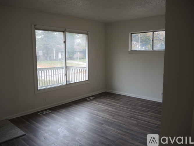A room with wooden floors and two windows overlooking a fence.