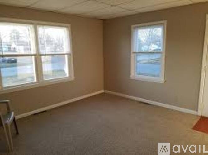 A room with a carpeted floor and two windows.