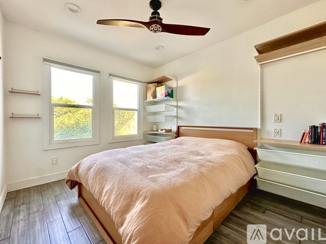 A bedroom with a bed, a ceiling fan, and a window with a view of greenery outside.
