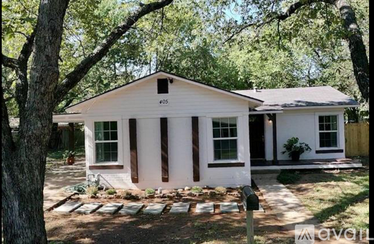A white house with a brown trim is surrounded by trees.
