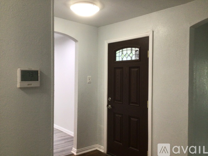 A brown door with a glass window is in a white hallway.