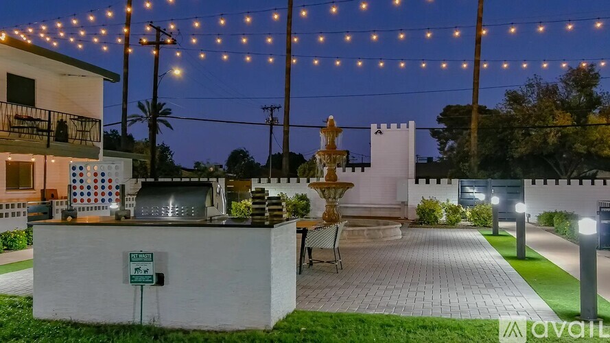 A white building with a fountain in front of it is lit up with string lights.