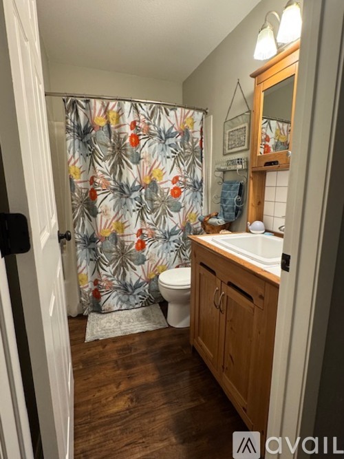 A bathroom with a floral shower curtain and wooden cabinets.