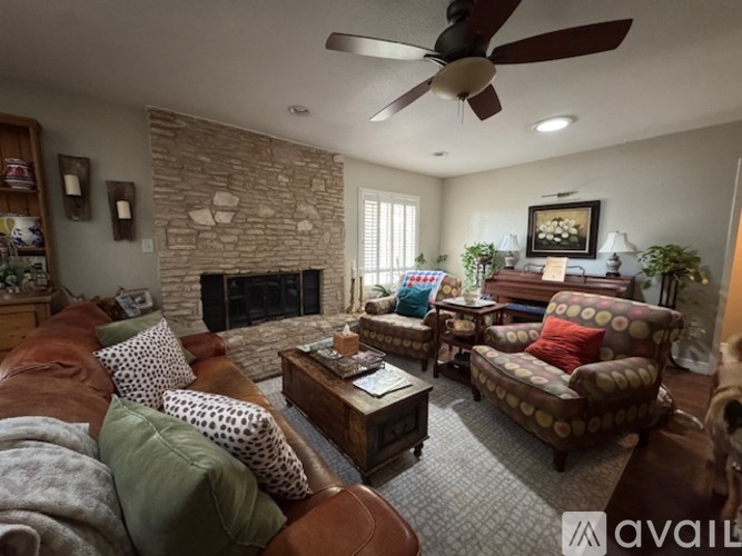 A living room with a stone fireplace and a ceiling fan.